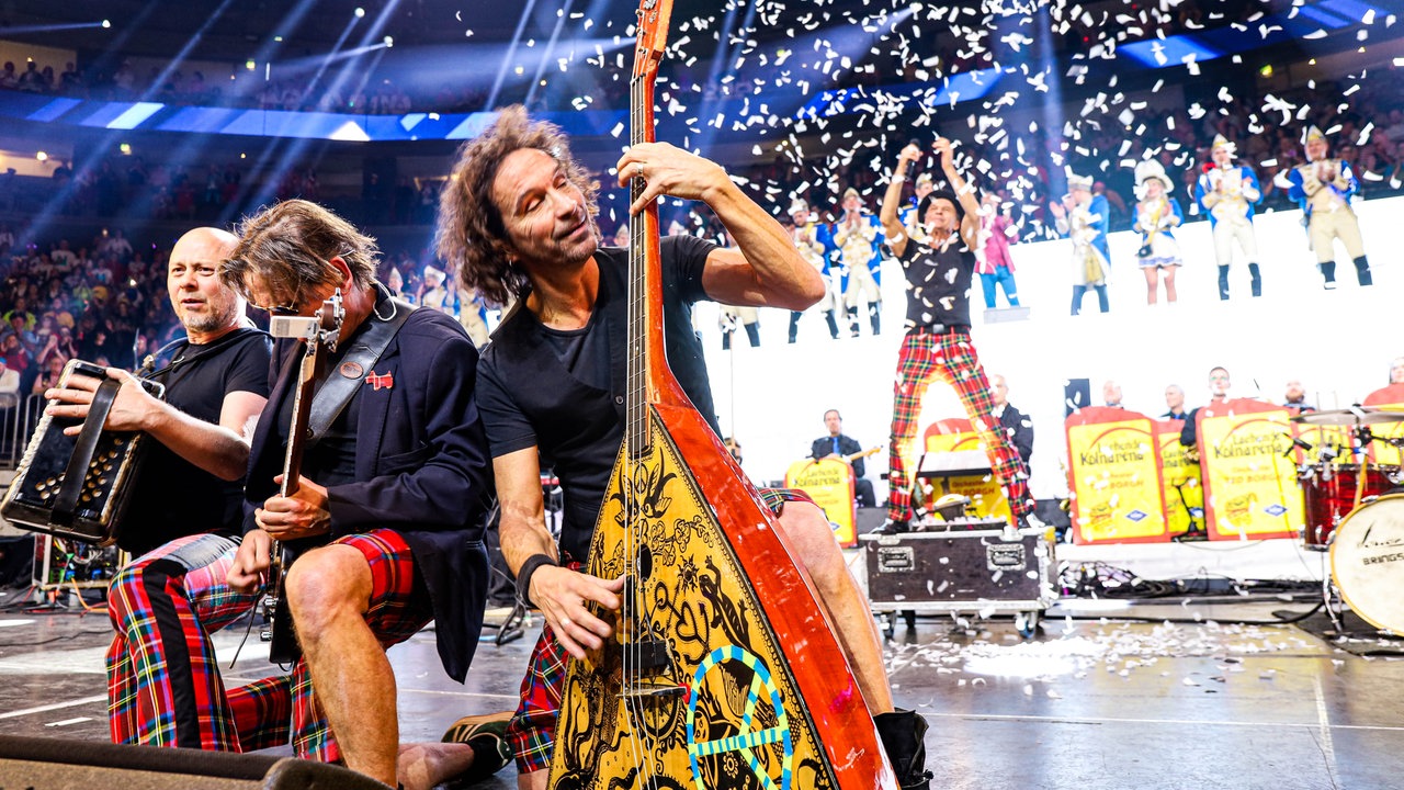 Lachende Köln Arena 2026: Stephan Brings von der Band Brings spielt die Gitarre, sein Bruder Peter feuert im Hintergrund eine Konfettikanone ab