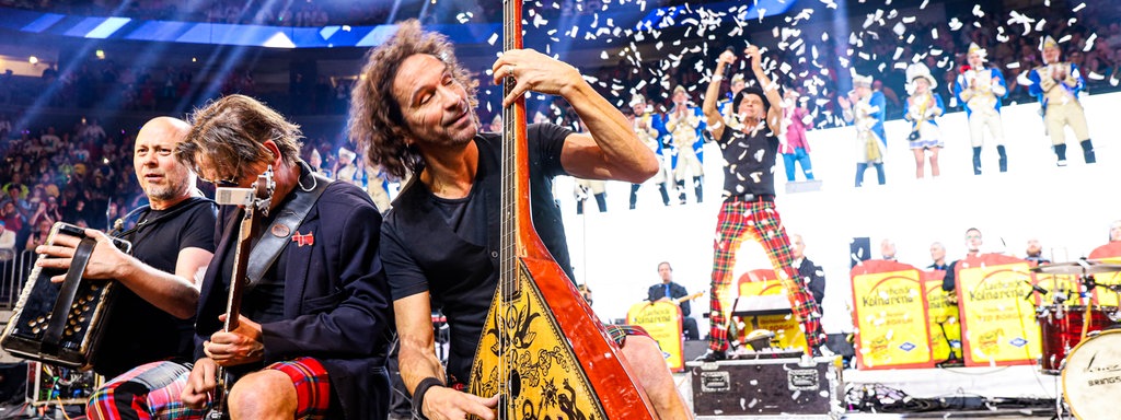 Lachende Köln Arena 2026: Stephan Brings von der Band Brings spielt die Gitarre, sein Bruder Peter feuert im Hintergrund eine Konfettikanone ab