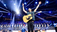 Lachende Köln Arena 2026: Der Sänger der Band Miljö hebt seine Arme zum Himmel und singt