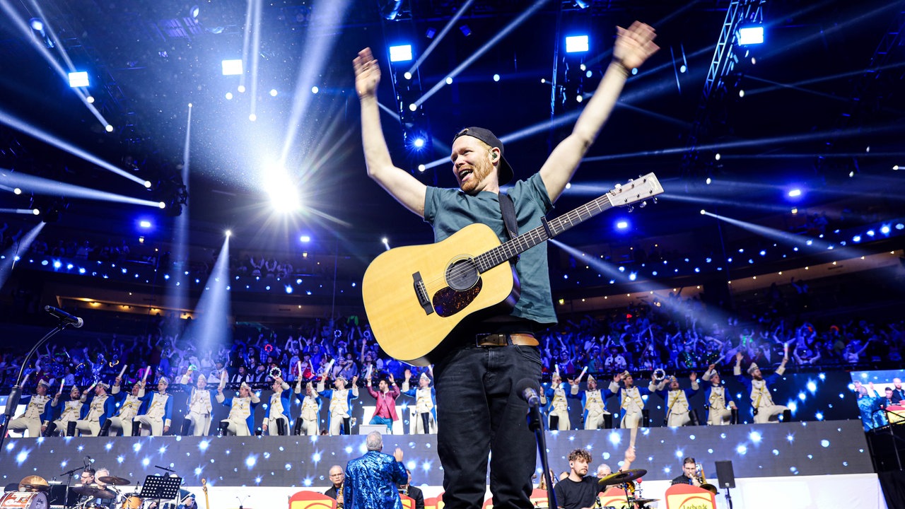 Lachende Köln Arena 2026: Der Sänger der Band Miljö hebt seine Arme zum Himmel und singt