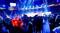 Lachende Köln Arena 2026: Ein Blick aus dem Publikum auf die Bühne. Im Vordergrund steht eine Frau mit einer leuchtenden Perücke.