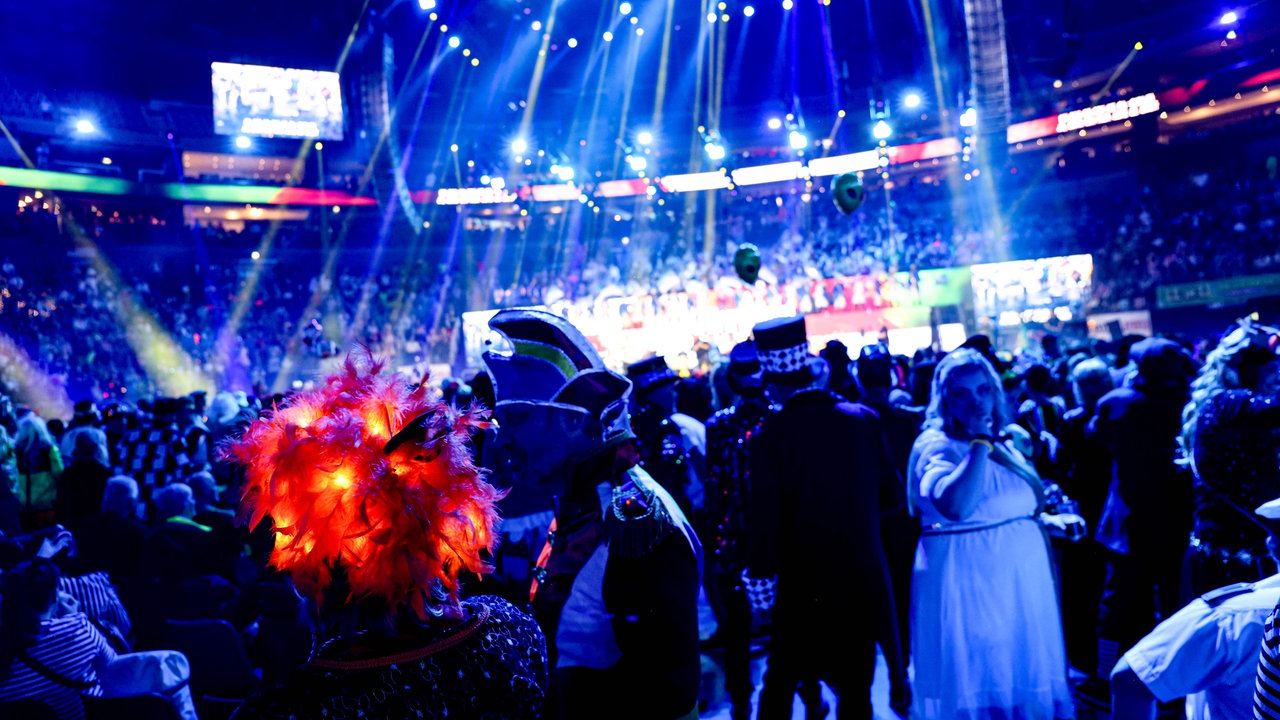 Lachende Köln Arena 2026: Ein Blick aus dem Publikum auf die Bühne. Im Vordergrund steht eine Frau mit einer leuchtenden Perücke.