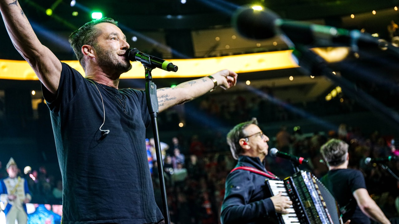 Lachende Köln Arena 2026: Der Sänger der Band Räuber steht mit ausgebreiteten Armen am Mikrofon und singt