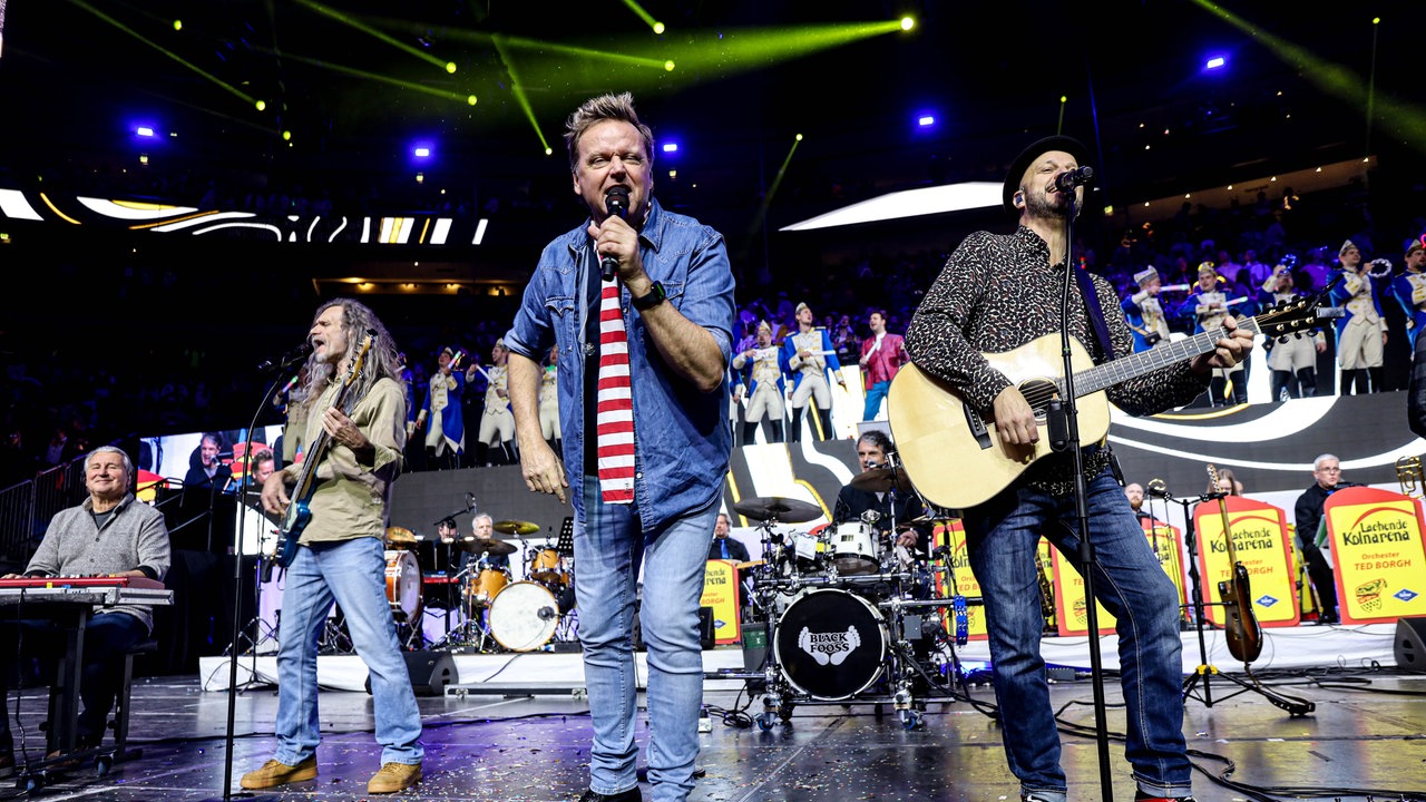 Lachende Köln Arena 2026: Die Band Bläck Fööss steht auf der Bühne. Der Frontmann singt mit einem Mikrofon vor dem Gesicht