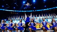 Lachende Köln Arena 2026: Ein blau-weißer Tanzcorps steht auf der Bühne. Fünf Mädchen knien, mehrere Männer werfen eine Tänzerin in die Höhe