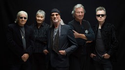 Die fünf Mitglieder der Band Deep Purple posieren nebeneinander vor einem schwarzen Hintergrund