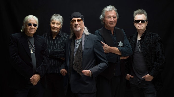 Die fünf Mitglieder der Band Deep Purple posieren nebeneinander vor einem schwarzen Hintergrund