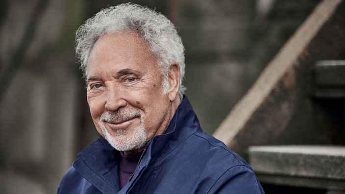 Tom Jones in blauer Jacke lächelt in die Kamera