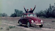 Ein Mann und eine Frau stehen in einem VW Käfer und winken aus dem Dach (1959)