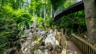 Das Felsenmeer in Hemer: Links im Bild sind Gestein und Gebüsch zu sehen, rechts gibt es einen hölzernen Fußweg und weiter oben eine Brücke