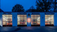 Außenansicht des Gerätehauses der Freiwilligen Feuerwehr Breckerfeld in der Dämmerung. Über den Eingängen stehen die Worte "retten, löschen, bergen, schützen". Die Löschfahrzeuge stehen im beleuchteten Gerätehaus. 