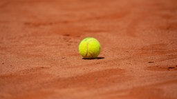 Ein gelber Tennisball liegt auf einem roten Ascheplatz