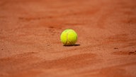 Ein gelber Tennisball liegt auf einem roten Ascheplatz
