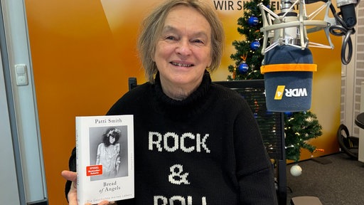 Elke Heidenreich im WDR 4 Studio: Sie hält das Buch "Bread of Angels" von Patti Smith hoch und trägt einen schwarzen Pulli mit der Aufschrift "Rock & Roll". 