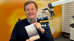Mike Altwicker im WDR 4-Studio mit dem Buch "Der Krabbenfischer" von Benjamin Wood in den Händen