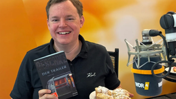 Mike Altwicker sitzt mit dem Buch "Der Trailer" von Linus Geschke und Muffins in der Hand im WDR 4 Studio.