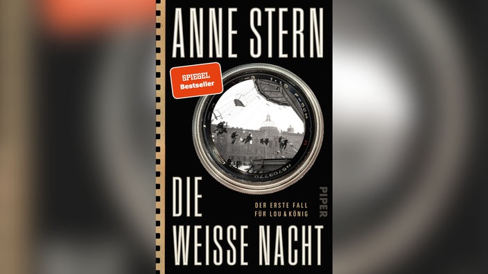 Buchcover von "Die weiße Nacht" von Anne Stern: Ein schwarzes Cover mit weißer Schrift. In der Mitte befindet sich ein schwarz-weiß Bild von Berlin, der Rahmen ist ein Kameraobjektiv, als würde man durch eine Kamera auf das Bild schauen.