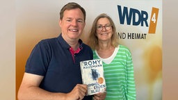 Ute Schneider und Mike Alwicker mit dem Buch "Himmelerdenblau" von Romy Hausmann in der Hand im WDR 4-Studio