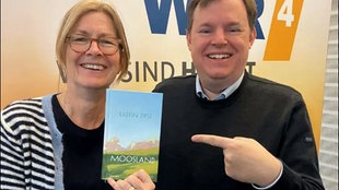 Ute Schneider und Mike Altiwicker halten das Buchcover "Moosland" von Katrin Zipse in die Kamera