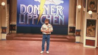 Jürgen von der Lippe steht 1987 vor dem Logo seiner Fernsehsendung "Donnerlippchen" im Studio