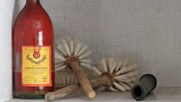 Eine Flasche Eulenspiegel Bohnerwachs und andere Utensilien stehen in einem alten Regal 