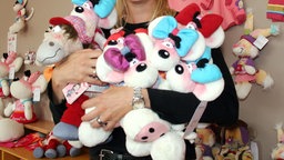 Mehrere Diddl-Mäuse und Diddl-Figuren in Form von Stofftieren in den Armen einer Frau