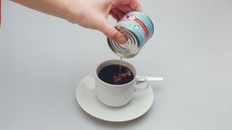Dosenmilch wird in eine Tasse Kaffee gegossen.