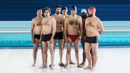 Männer in Badehose und -mütze stehen in einer Schwimmhalle