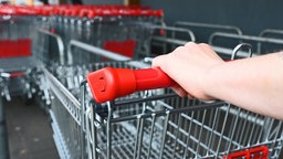Eine Einkäuferin schiebt einen Einkaufswagen vor einem Supermarkt