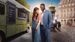 Eine Straße in Paris: In der Mitte des Bildes befinden sich Abel (Omar Sy) und Marion (Sara). Sie steht mit dem Rücken zu ihm, schaut ihn aber über die Schulter an, er schaut sie ebenfalls an. Fotografen im Hintergrund fotografieren das Paar.