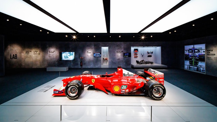 Ein Ausstellungsraum, in der Mitte steht ein roter Ferrari-Rennwagen. 