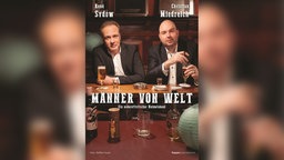 René Sydow und Christian Miedreich des Kabaretts "Männer von Welt" sitzen mit Bier, Schnaps und Zigarre am Tisch in einer Kneipe