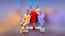 Die Darsteller des Stücks "Vollversammlung im Neurosengarten" vor einem Neonschriftzug "New York"