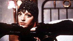 Szene aus dem Film "Cabaret" (1972): Liza Minelli lehnt im Kostüm über einem Bettgestell