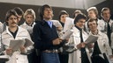 Die Fußballnationalmannschaft 1978 mit Udo Jürgens bei Aufnahmen zum WM-Song "Buenos Dias Argentina". Die Nationalspieler stehen in Trainingsjacken um Udo Jürgens herum, alle halten Textzettel in der Hand und singen. 