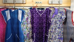 Dederon-Schürzen in verschiedenen Designs auf Kleiderbügeln.