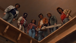 Eine Szene aus "Stranger Things": Mike, Lucas, Nancy, Steve, Jonathan und Dustin gespielt von Finn Wolfhard, Caleb McLaughlin, Natalia Dyer, Joe Keery, Charlie Heaton und Gaten Matarazzo stehen auf einer Empore. Steve hält eine Kettensäge.