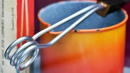 Ein Tauchsieder, der auf einer orangenen Tasse abgelegt ist.