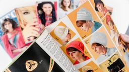 Ein aufgeschlagener Katalog für Damenhüte. Auf dem Tisch im Hintergrund liegen weitere Kataloge. 