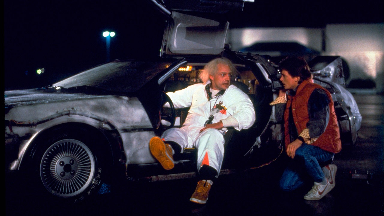 Szene aus dem Film "Zurück in die Zukunft": Schauspieler Michael J. Fox und Christopher Lloyd unterhalten sich vor dem Zeitreise-Auto