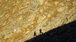 Schatten von zwei Alpinisten im Aufstieg an einem Grat 