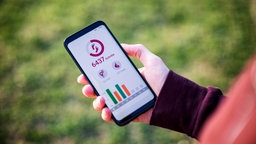 Ein Mann hält ein Handy und nutzt eine Fitness-App, die Schritte zählt