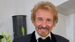 Thomas Gottschalk im schwarzen Anzug mit schwarzer Fliege. Er lächelt in die Kamera. 