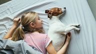 Ein blondes Mädchen liegt mit ihrem Hund im Bett und schläft