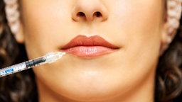Man sieht die untere Hälfte eines Frauengesichts und es wird eine Spritze an die Lippe gehalten.