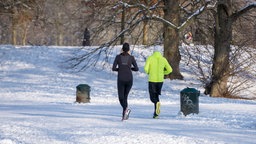 Zwei Jogger in einem verschneiten Park mit kahlen Bäumen
