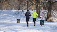 Zwei Jogger in einem verschneiten Park mit kahlen Bäumen