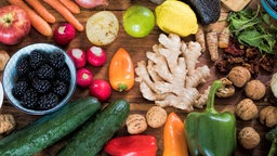 Frisches Obst, Gemüse und Nüsse liegen bunt gemischt auf einem Holztisch