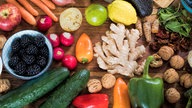 Frisches Obst, Gemüse und Nüsse liegen bunt gemischt auf einem Holztisch