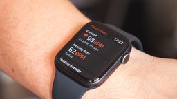 Nahaufnahme eines Handgelenks mit einer Smartwatch. Auf dem Display wird die Herzfrequenz angezeigt.